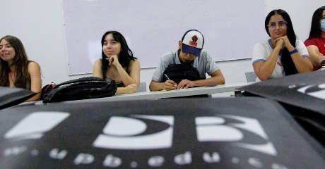 Estudiantes en aula de clase, se ve un cuaderno de la UPB en primer plano
