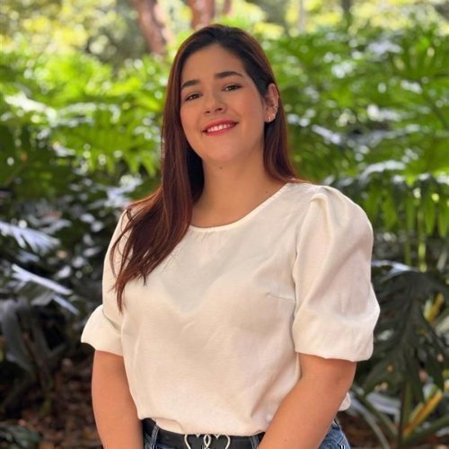 Retrato de Maria Isabel Fernández Molina sonriendo, con blusa blanca y fondo de vegetación verde.